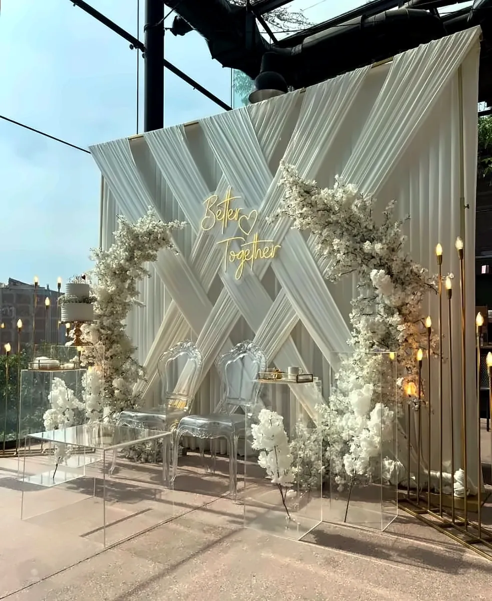 Better Together neon sign on a white draped backdrop with white floral arch and candle stands by Mayur Events Bilaspur