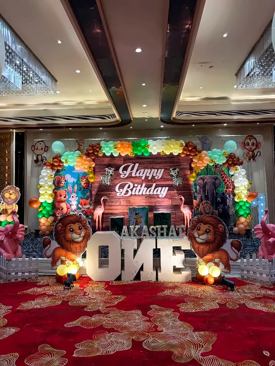 Jungle theme first birthday stage decoration with lion cut-outs, balloons and ONE letters in a banquet hall by Mayur Events Bilaspur